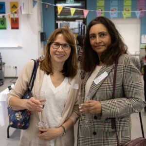 Two women posing with drinks at an indoor social event, smiling toward the camera.