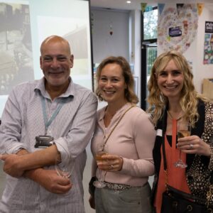 Three adults posing for a photo at an indoor event, each holding wine glasses and smiling at the camera.