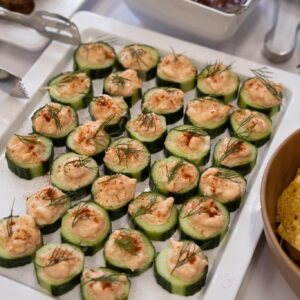 Tray of cucumber bites topped with creamy dip, dill sprigs, and a dusting of paprika on a white platter.
