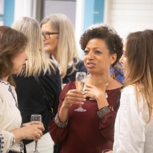 Group of women in conversation at a social event, holding champagne flutes indoors.
