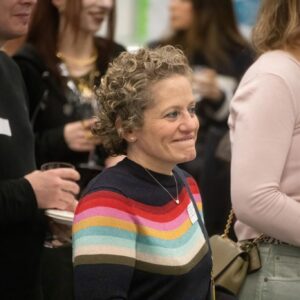 Smiling woman with short curly gray hair wearing a multicolor striped sweater at a social gathering.
