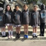 Five students stand on stone steps outdoors, wearing matching dark hoodies with a 'Digital Leaders' logo on the back and a gear/hand design on the front; some face the camera, others have their backs turned.