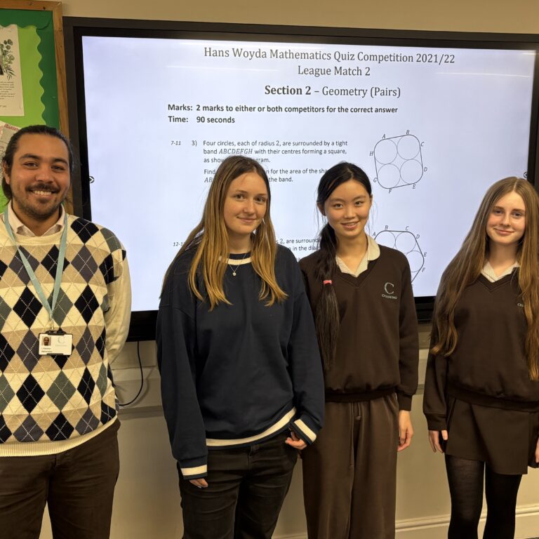 Four students stand in a classroom in front of a large screen showing a math quiz slide.