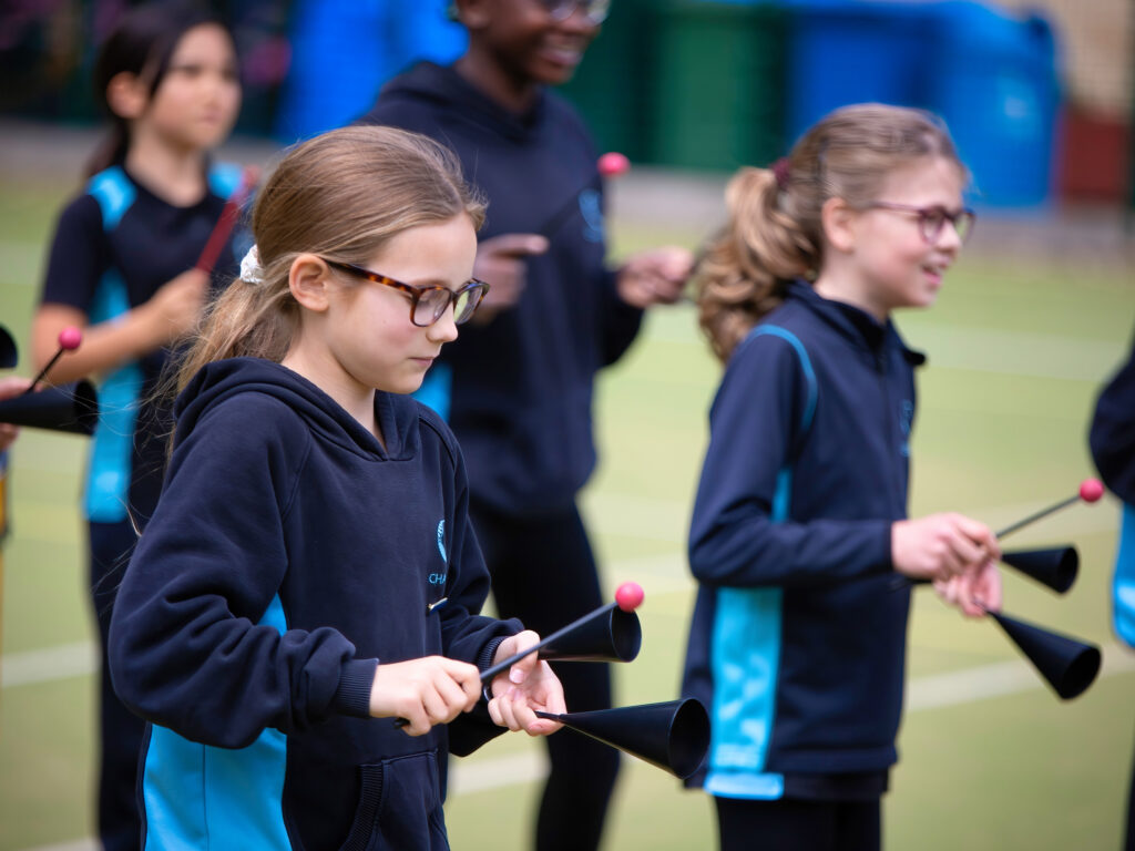 Group of children in navy uniforms practicing baton twirling with pink-tipped batons on a sports field.