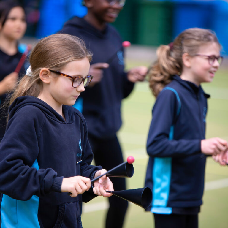 Group of children in navy uniforms practicing baton twirling with pink-tipped batons on a sports field.