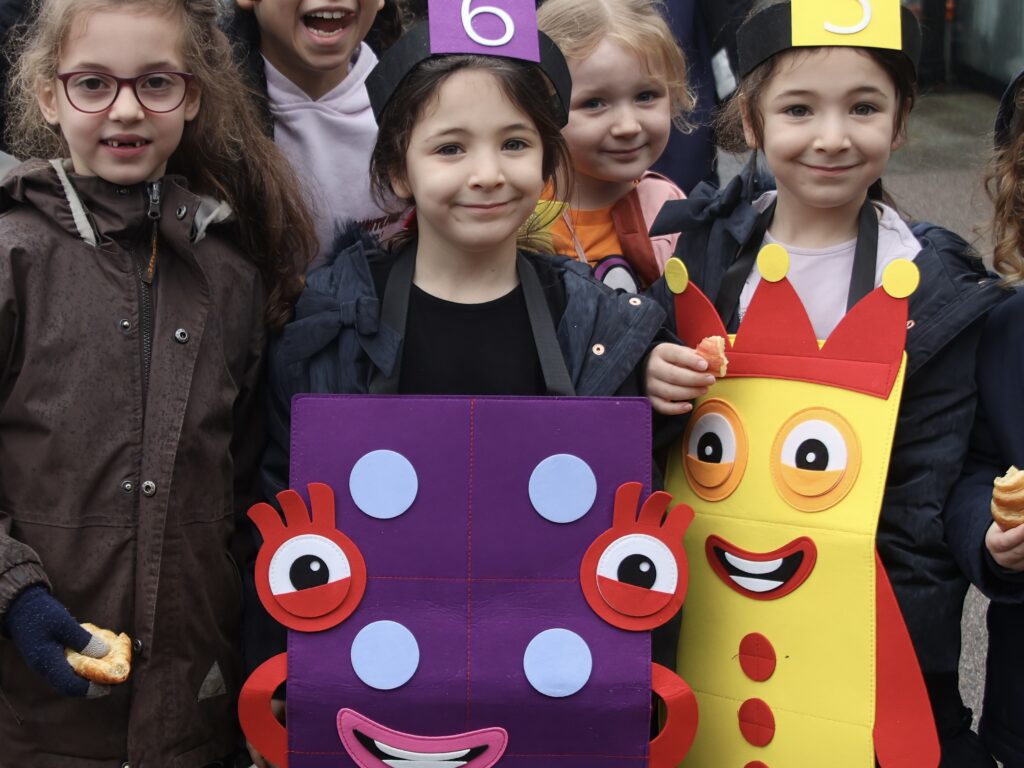 Group of children in colorful cardboard crayon costumes (purple and yellow) posing for a photo, smiling at the camera.