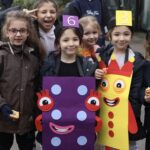 Group of children in colorful cardboard crayon costumes (purple and yellow) posing for a photo, smiling at the camera.