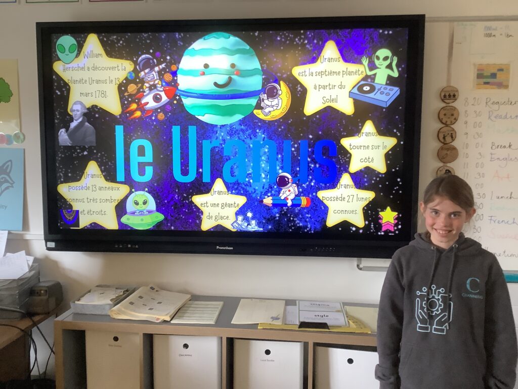 Colorful classroom display about Uranus with planets, astronauts, and a smiling planet on a space-themed poster; a student stands nearby.