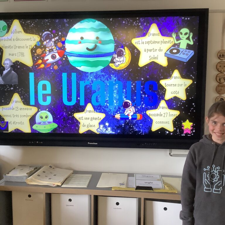 Colorful classroom display about Uranus with planets, astronauts, and a smiling planet on a space-themed poster; a student stands nearby.