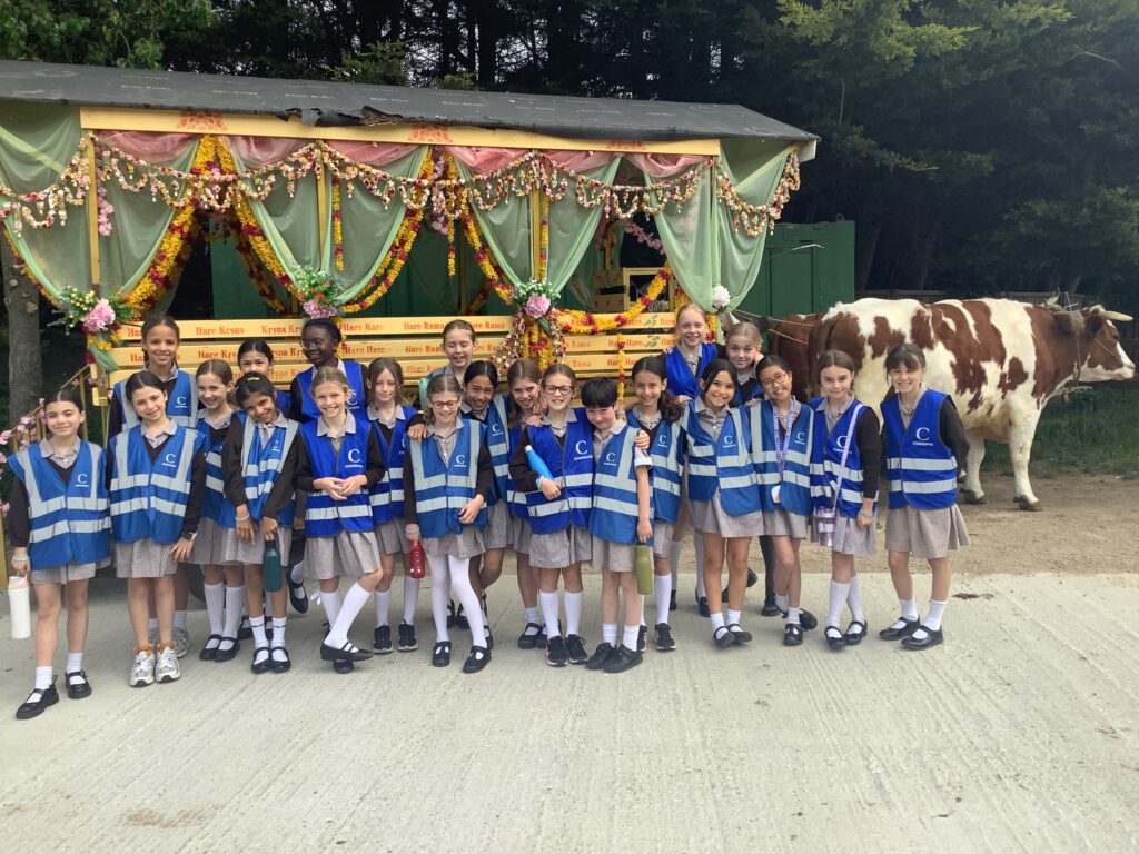 Group of schoolchildren in blue vests posing in front of a flower-decorated parade float with cows nearby at a rural event.