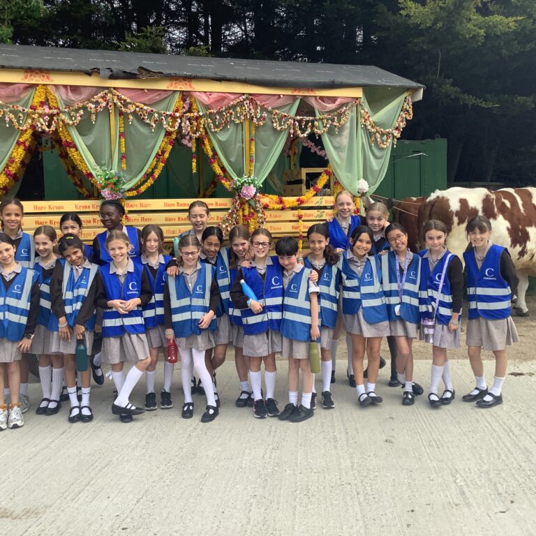 Group of schoolchildren in blue vests posing in front of a flower-decorated parade float with cows nearby at a rural event.